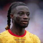 Close-up portrait of a Black male soccer player with braided hair, wearing a bright yellow England vs Ghana jersey with red collar (June 23, 2026).
