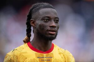 Close-up portrait of a Black male soccer player with braided hair, wearing a bright yellow England vs Ghana jersey with red collar (June 23, 2026).