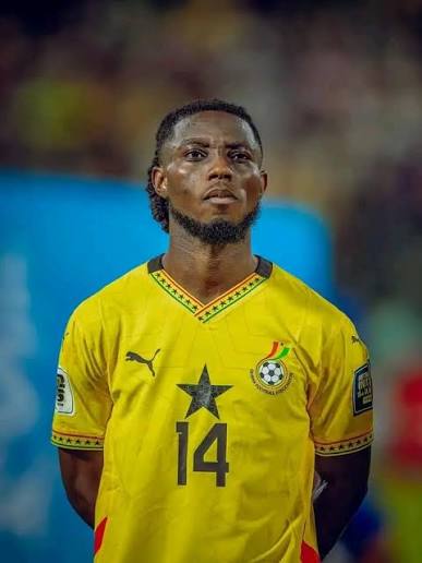 Ghana national football team player wearing a yellow jersey with number 14, standing on the field with a focused expression.