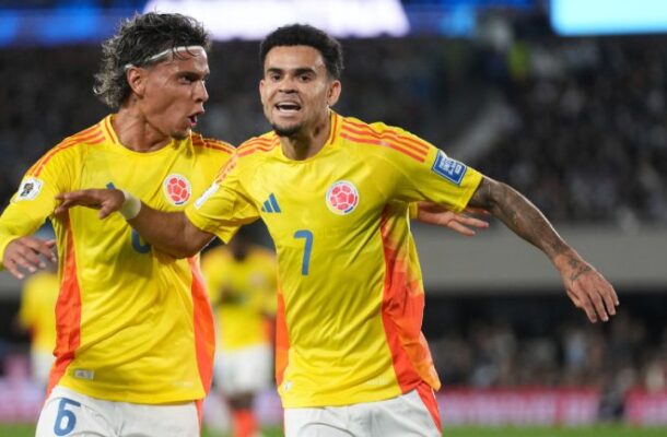 Two Colombian national team players in yellow jerseys celebrate on the soccer field, arms around each other after a goal or play.