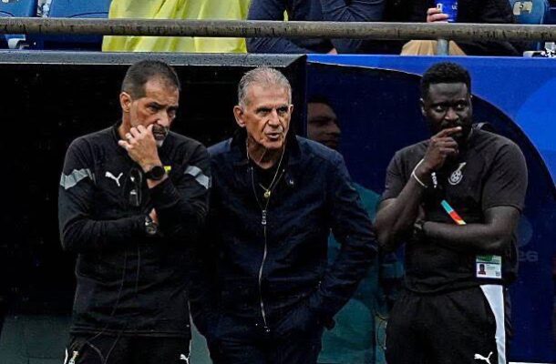IMG_1185 | Ghanaguardian.com Three men stand on a stadium sideline, two in black athletic gear flanking a man in a dark zip jacket, all looking serious.