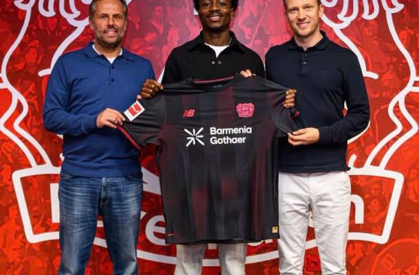 IMG_1189 | Ghanaguardian.com Three men pose indoors holding a dark red and black soccer jersey with sponsor logos (Barmenia Gothaer) in front of a red wall featuring a large white club crest and the number 1904.