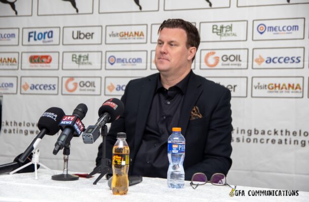IMG_1201 | Ghanaguardian.com Man in a dark blazer seated at a press conference table with multiple microphones in front of him, sponsor logos on a backdrops behind him with water bottles on the table.