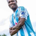 Young man in a blue and white striped soccer jersey smiles with arms crossed.