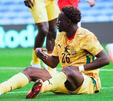IMG_1226 | Ghanaguardian.com Soccer player in a yellow kit with number 26 sitting on the grass during a match, with arms gesturing and other players blurred in the background.