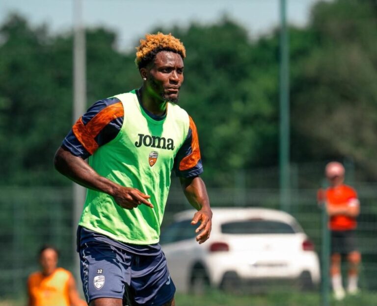 Soccer player with blond hair in a neon green bib running on a training field.