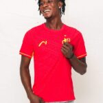 Smiling man in a red Portugal soccer jersey standing against a white backdrop.