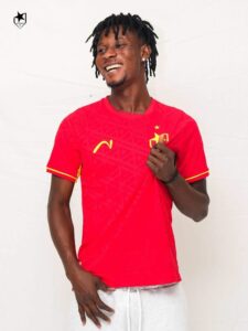 Smiling man in a red Portugal soccer jersey standing against a white backdrop.