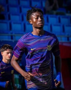 Young male footballer in a purple FC Barcelona training jersey running on a stadium pitch with blue seats in the background