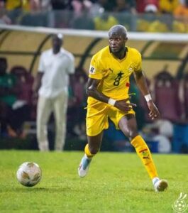 Soccer player in yellow uniform dribbling the ball on a green field during a match.
