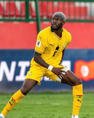 Footballer in a bright yellow kit crouches on a grass pitch, ready to receive or control the ball during a match.