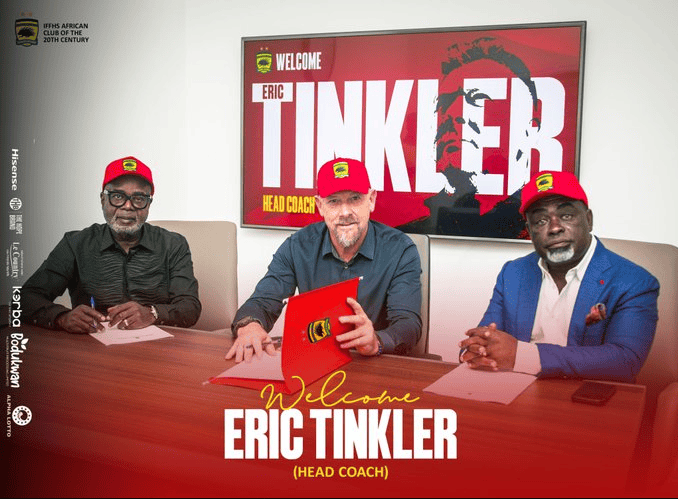 Three men in red caps sit at a conference table signing documents, with a large screen behind them that reads 'Welcome Eric Tinkler (Head Coach)'.