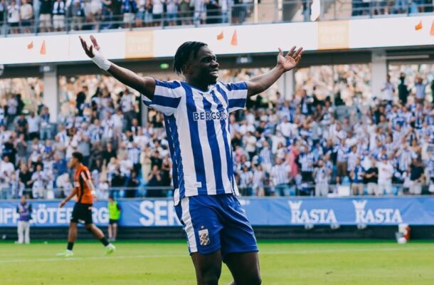 IMG_1310 | Ghanaguardian.com Soccer player in a blue-and-white striped kit with orange cleats raises arms in celebration on a green pitch as a full stadium cheers behind him.