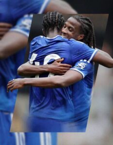 Two soccer players in blue jerseys hug in celebration on the field, smiling.