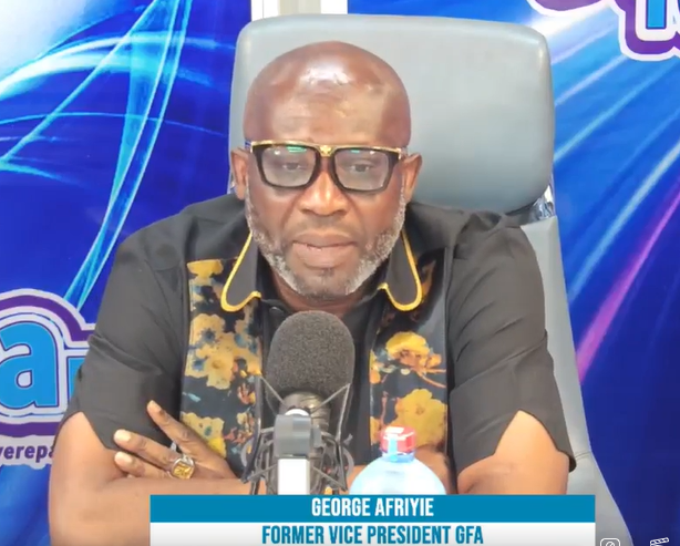 Man wearing glasses and a black shirt with yellow floral accents sits at a microphone on a studio desk; caption shows 'George Afriye, Former Vice President GFA'.