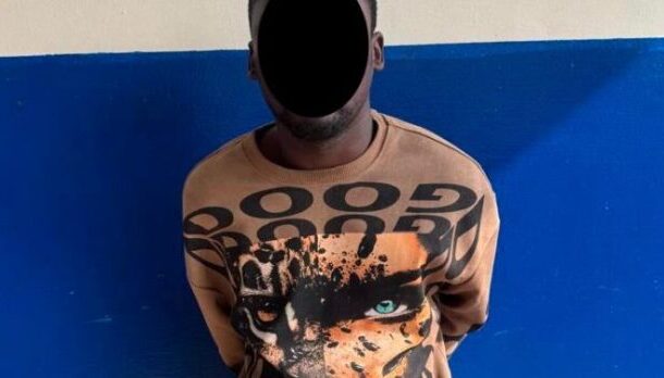 Person with face obscured by a black shape stands against a blue wall wearing an orange shirt with a tiger graphic.