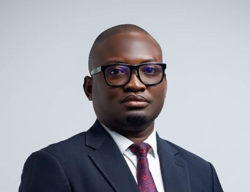 Professional headshot of a man in a navy suit, white shirt, maroon tie, wearing glasses, looking at the camera.