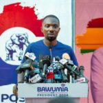 Man in a blue shirt speaking at a podium crowded with microphones at a campaign event; banner reads BAWUMIA FOR PRESIDENT 2024