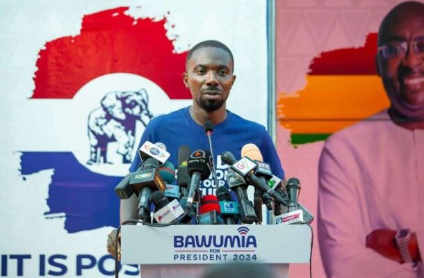 NPPs-Dennis-Miracles-Aboagye | Ghanaguardian.com Man in a blue shirt speaking at a podium crowded with microphones at a campaign event; banner reads BAWUMIA FOR PRESIDENT 2024