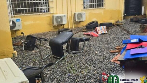 National-Peace-Council-696x348 | Ghanaguardian.com Outdoor cluttered courtyard with discarded chairs, tires, and colorful boards scattered on gravel next to a yellow building.
