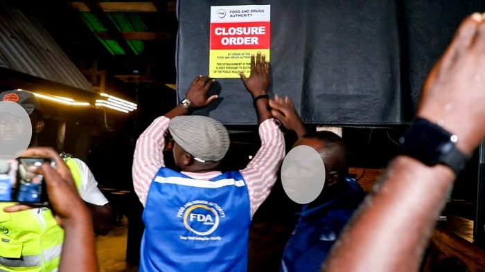 Staff with an FDA vest posts a red 'Closure Order' sign on a doorway during an inspection.