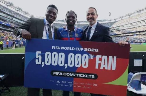 Screenshot 2026-07-01 155532 | Ghanaguardian.com Three men pose with a large colorful banner that reads 'FIFA World Cup 2026 5,000,000th Fan' at a stadium, celebrating the milestone together.