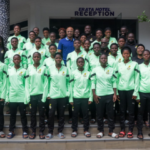 Group of young athletes in neon green jackets posing for a team photo on hotel steps in front of a reception sign.