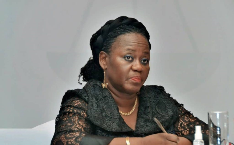 African American woman seated at a table in a black lace outfit, holding a pen and looking thoughtful during a formal meeting.