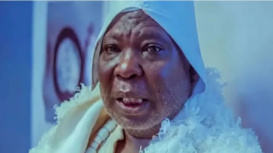 Close-up of a man wearing a white headscarf and robe under blue lighting, looking at the camera with a slight smile.