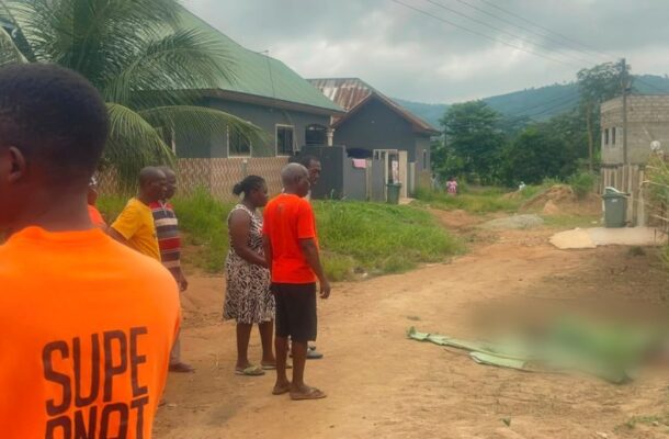 WhatsApp-Image-2026-07-05-at-105651-AM-1140x570 | Ghanaguardian.com Group of people in orange shirts gather on a dusty village street; a covered body lies blurred on the ground nearby.