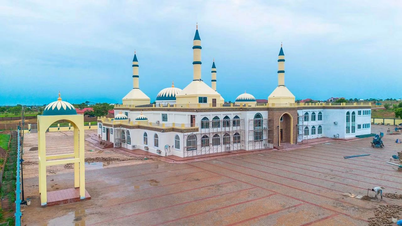 WhatsApp Image 2026-07-06 at 115552 2 | Ghanaguardian.com Large mosque complex with cream and gold domes, four tall minarets, and a spacious paved courtyard; some scaffolding at the entrance suggesting ongoing construction.