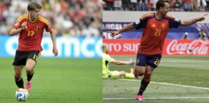 Two soccer players in red Belgium kits share the frame: left player #17 dribbles the ball, right player #21 points and runs forward as a goalkeeper lies in the background.