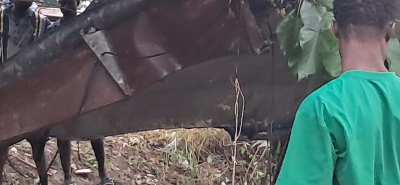 Person in a green shirt seen from behind, standing beside a large, rusted boat hull on dry ground