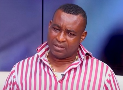 Wontumi | Ghanaguardian.com Man in a pink and white striped shirt looks puzzled while seated indoors, wearing a clip-on mic at a talk-show setting.