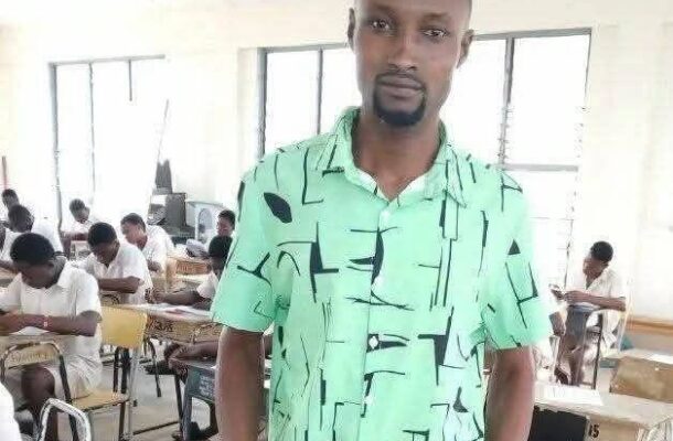 Portrait of a young man in a bright green geometric-pattern shirt standing in a classroom, with students seated at desks in the background.