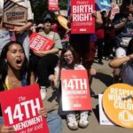 Diverse group of protesters at an outdoor rally holding signs about reproductive rights, including a front-left sign reading 'The 14th Amendment'.