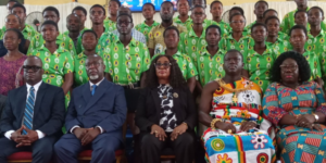Group portrait at a formal event: five seated adults in front row, with a large crowd in matching green shirts behind them.