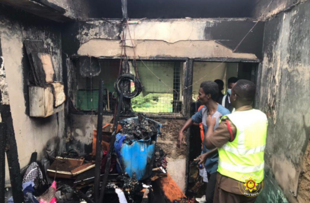 Post-fire scene inside a burnt room with charred walls and debris; responding personnel in a high-visibility vest assess the damage.