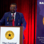 A man with glasses and a beard in a navy suit delivering a speech at a wooden podium with the Bank of Ghana seal, supported by red curtains in the background.