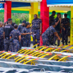 Group of uniformed personnel under a colorful canopy, inspecting rows of carts with bright yellow handles.