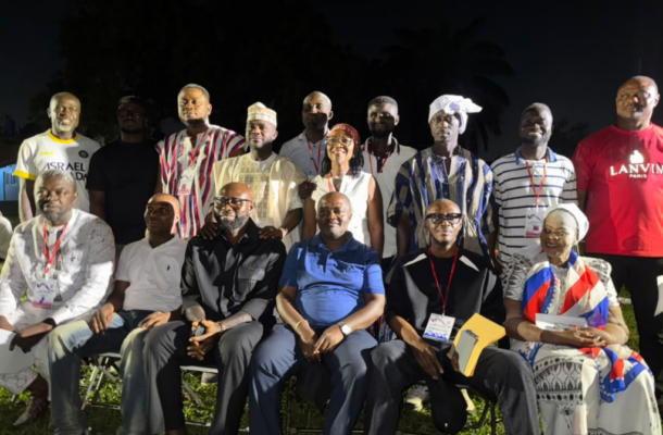 Group of 15 people posing outdoors at night, some in traditional attire and badges, seated in front row and standing behind them.