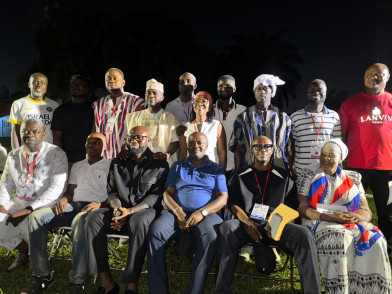 Group of 15 people posing outdoors at night, some in traditional attire and badges, seated in front row and standing behind them.