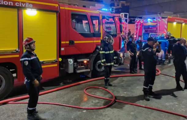 image-669-696x391 | Ghanaguardian.com Firefighters in gear beside red fire trucks on a wet street at night, hoses laid out.