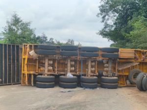 Yellow truck trailer overturned on its side in a yard, with wheels stacked along the frame.