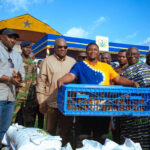 Group of men at a market event in Ghana, a man in blue and yellow holds a blue crate of fish