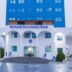 National Investment Bank building with white arches and a blue sign, entrance steps, and a tall blue glass office tower behind it.