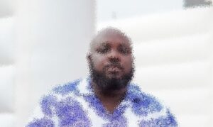 Bearded man in a light blue patterned shirt seated indoors, facing the camera.