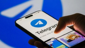 Hand holding a smartphone displaying the Telegram app logo on screen.