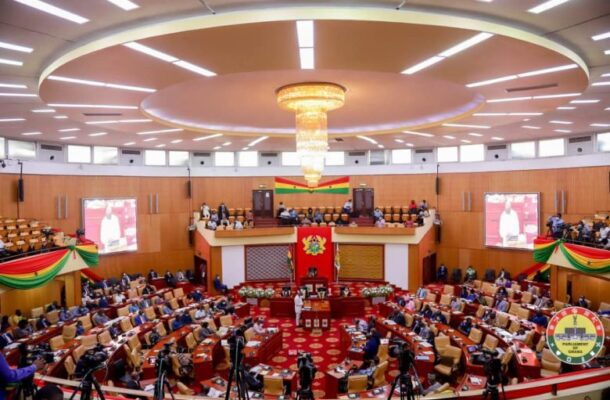 parliament-e1752739834548 | Ghanaguardian.com Parliamentary chamber with a central podium, curved seating, and a grand chandelier overhead, decorated with flags and banners.