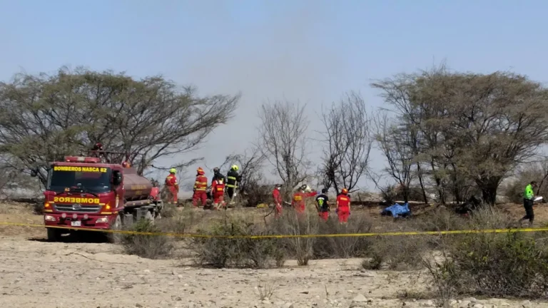 Firefighters in red gear and a red fire truck on a dry desert site, with yellow caution tape marking off the scene.